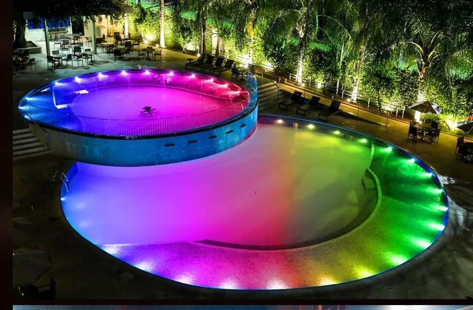 A round pool lit pink and green at night, with palms behind it